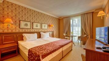 A hotel room with a large bed, a desk with a TV, a chair, and a small table.