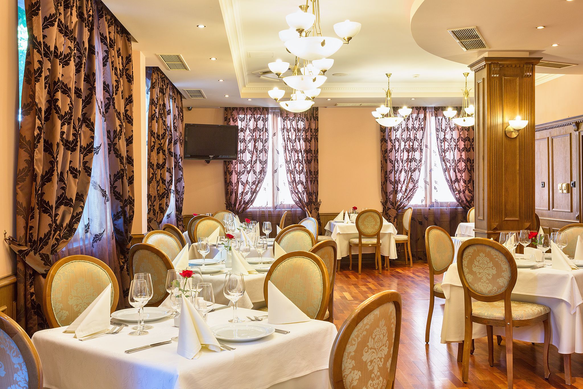 Een restaurant met meerdere eettafels, met kroonluchters en gordijnen.