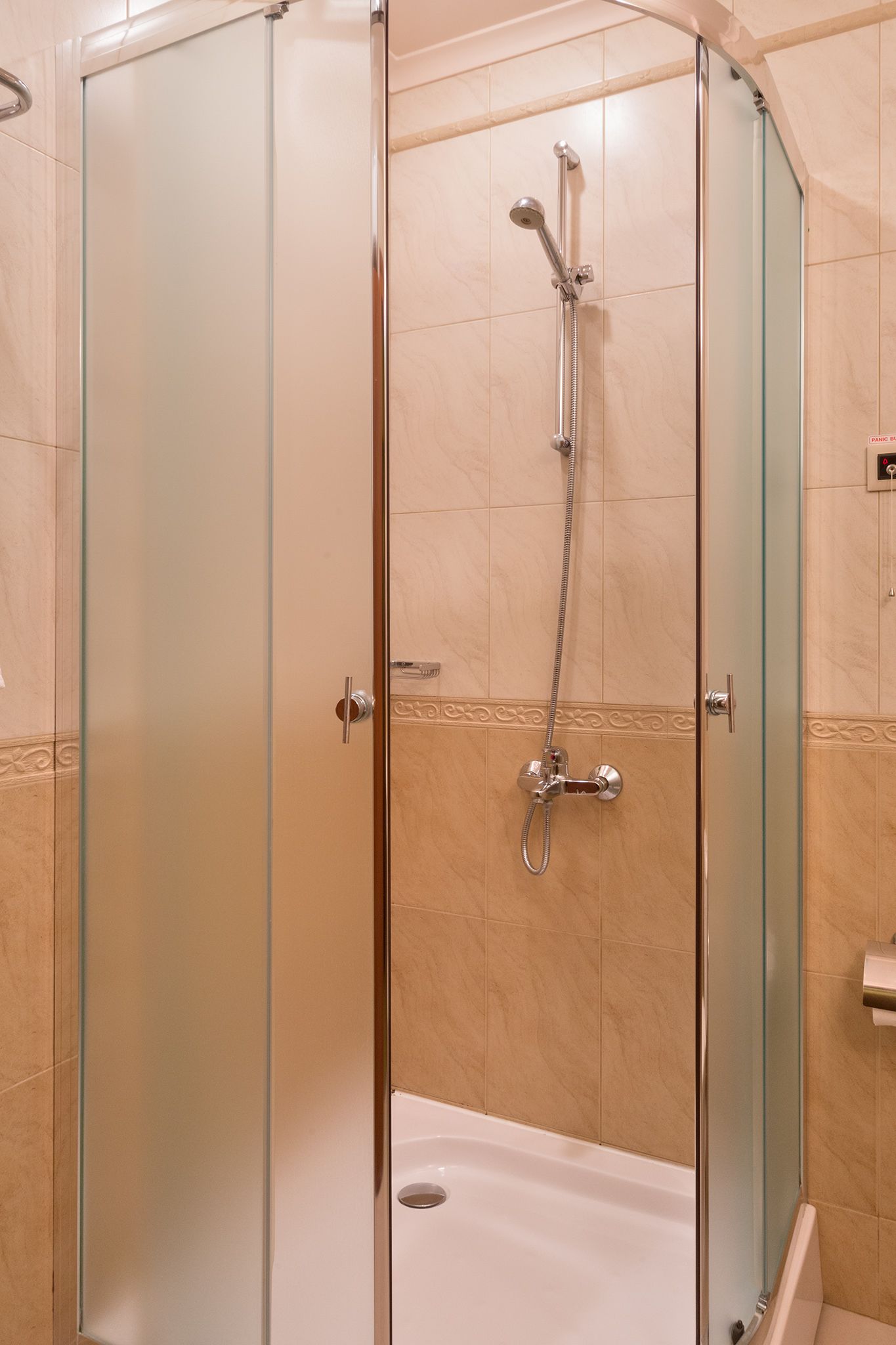 Ducha con cerramiento de vidrio, cabezal de ducha de mano y grifo empotrado.