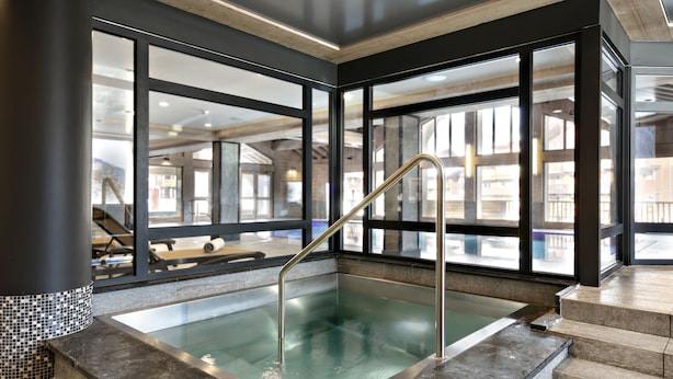 Un'area piscina moderna, interna, con pareti divisorie in vetro, una scala in metallo e un pavimento in pietra.