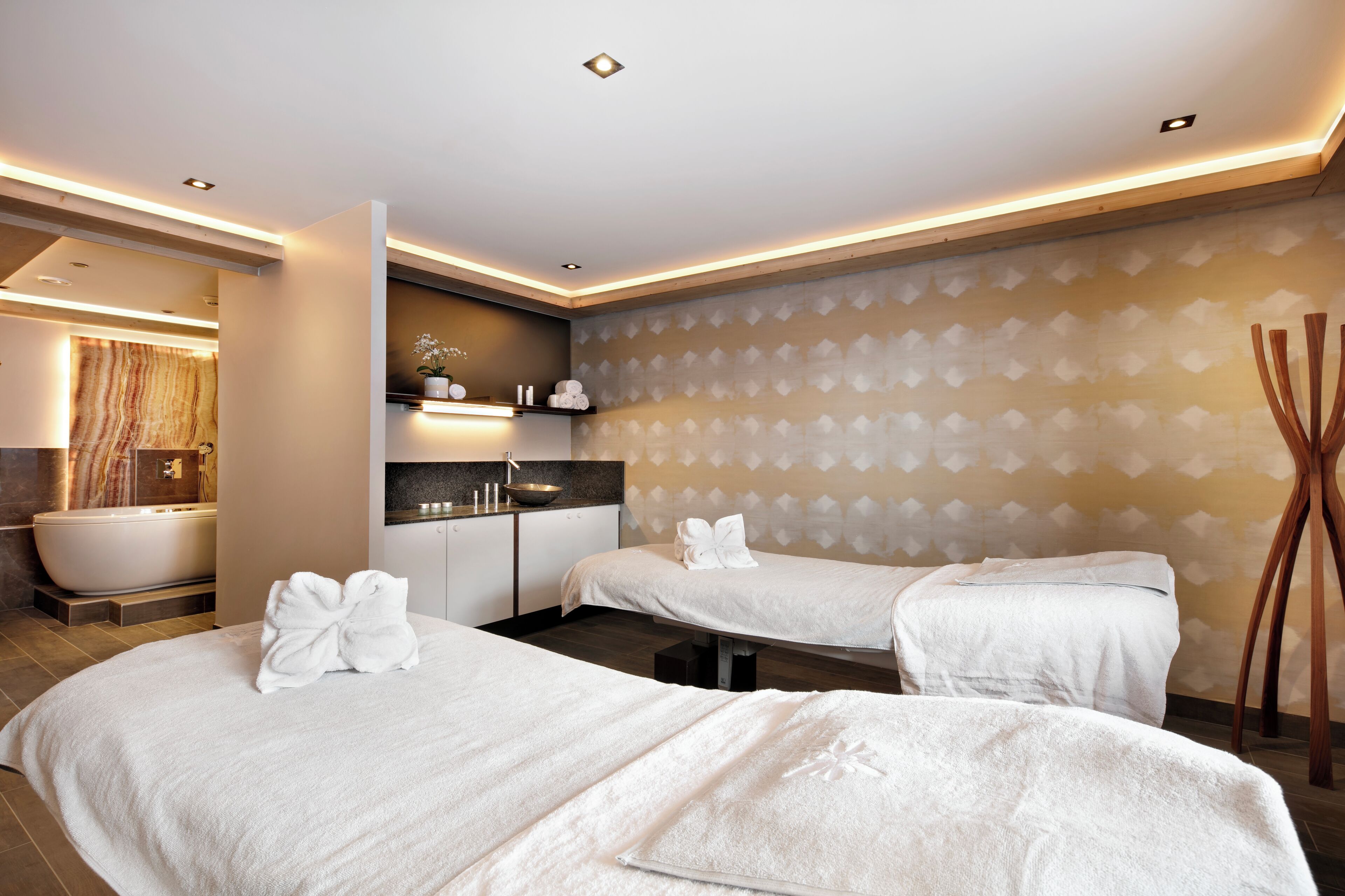 A modern hotel room with two beds, a bathtub, a vanity, and a patterned wall.