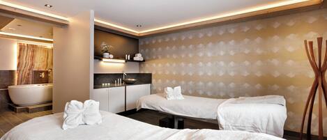 A modern hotel room with two beds, a bathtub, a vanity, and a patterned wall.
