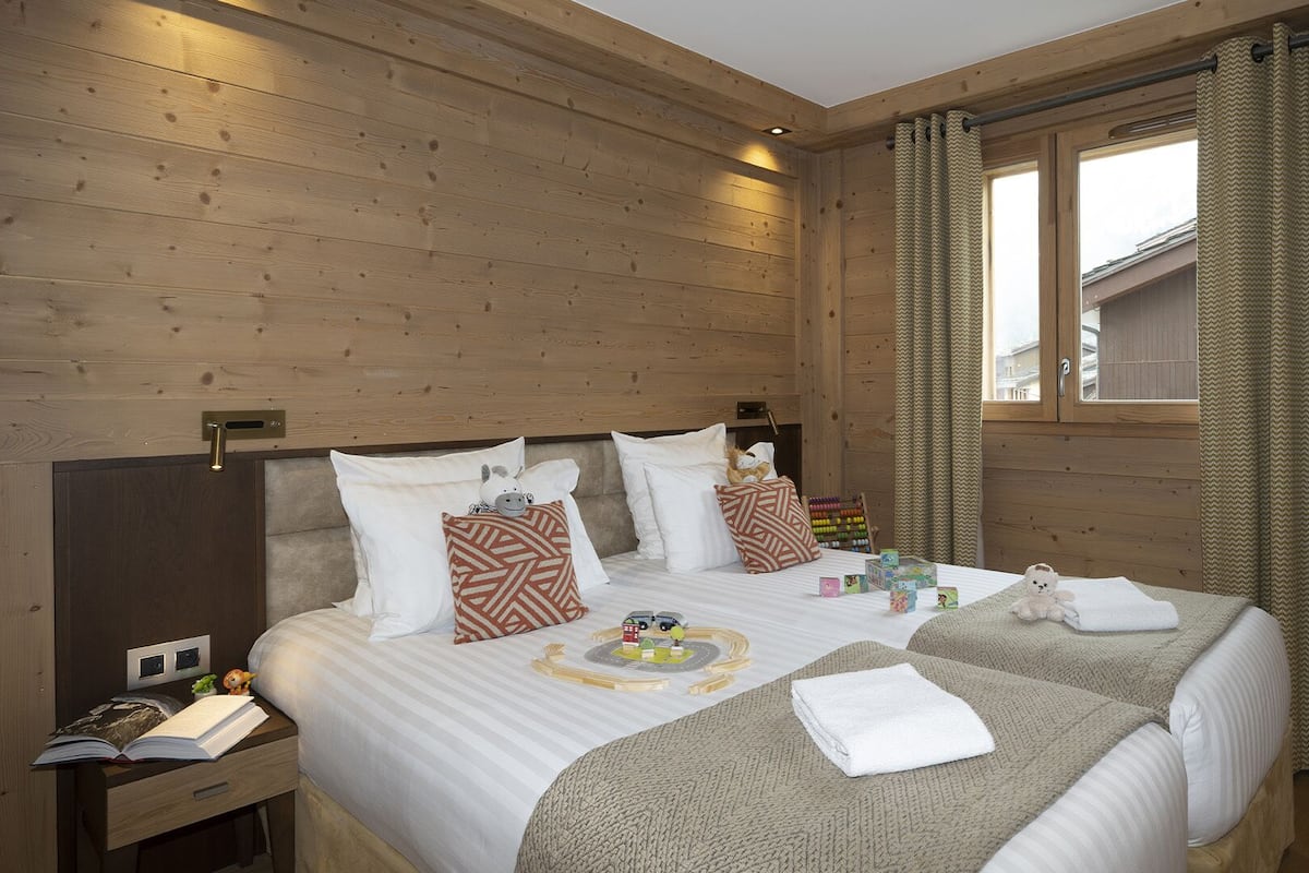 Una habitación con paneles de madera, una cama, una mesita de noche y una ventana con cortinas.