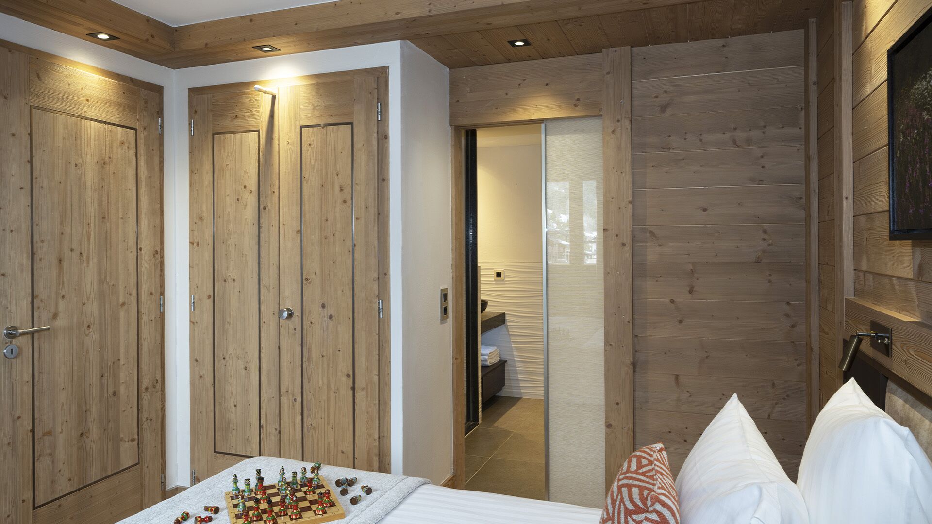 A bedroom with wooden walls, a bed with pillows, and a chessboard on the floor.