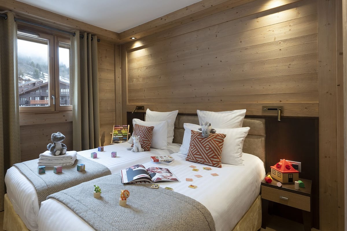 Una habitación acogedora con dos camas, paredes de madera, un ventanal con cortinas y una mesita de noche con lámpara.