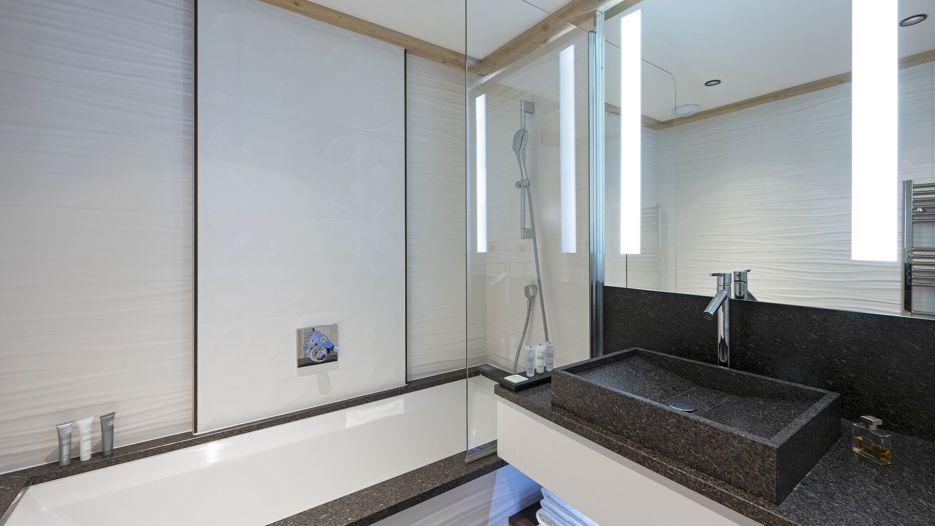 A modern bathroom with a glass shower enclosure, a granite countertop sink, and a large mirror.