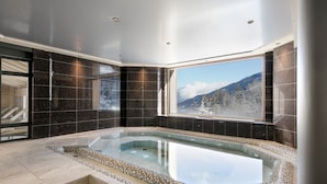 Un bagno moderno con una grande vasca da bagno, pareti piastrellate scure e una finestra con vista sulle montagne.