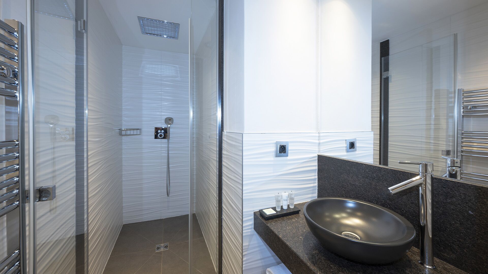 A modern bathroom with a glass-enclosed shower, a large mirror, and a black vessel sink.