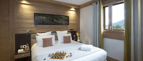Un dormitorio con techo de madera, una cama grande con ropa blanca, un tablero de ajedrez y una ventana con cortinas.