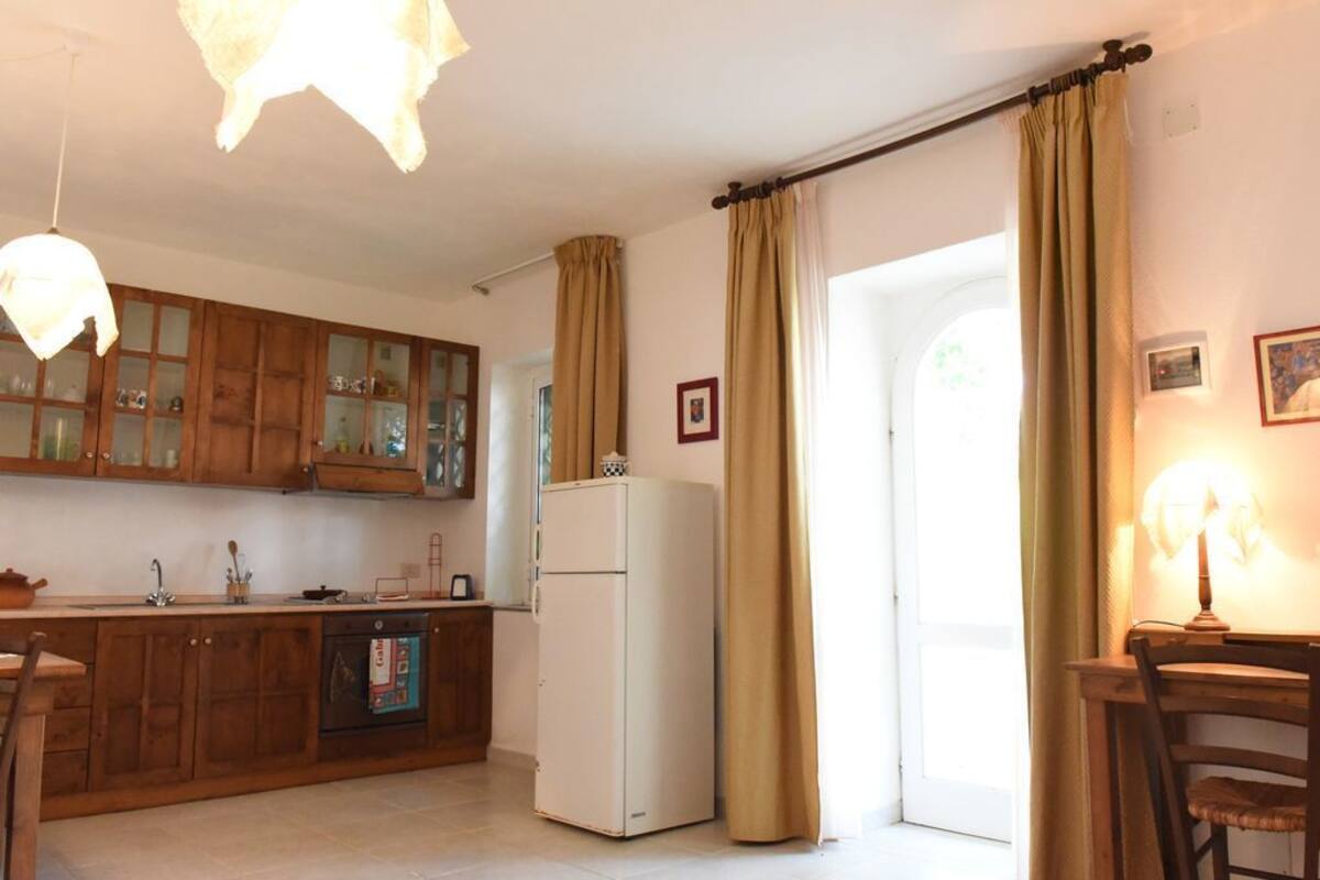 A kitchen with wooden cabinets, a refrigerator, a dining table with chairs, and a hanging light fixture.