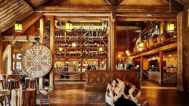 A rustic interior with wooden beams, a large wooden clock, and shelves filled with pottery. - La Cite suspendue (Plailly)