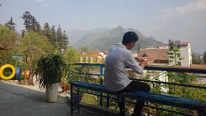 A man sitting on a blue bench overlooking a mountainous landscape with houses and trees in the background. - Sapa Tatu Homestay (Sa Pa)