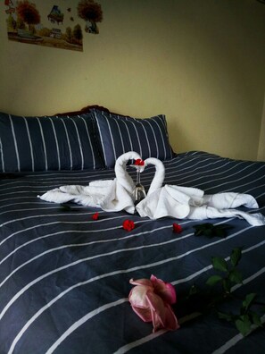 A bed with striped bedding, a heart-shaped towel arrangement, and a single rose.
