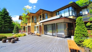 Una casa moderna de dos pisos con terraza de madera, ventanas grandes y mobiliario para exterior.