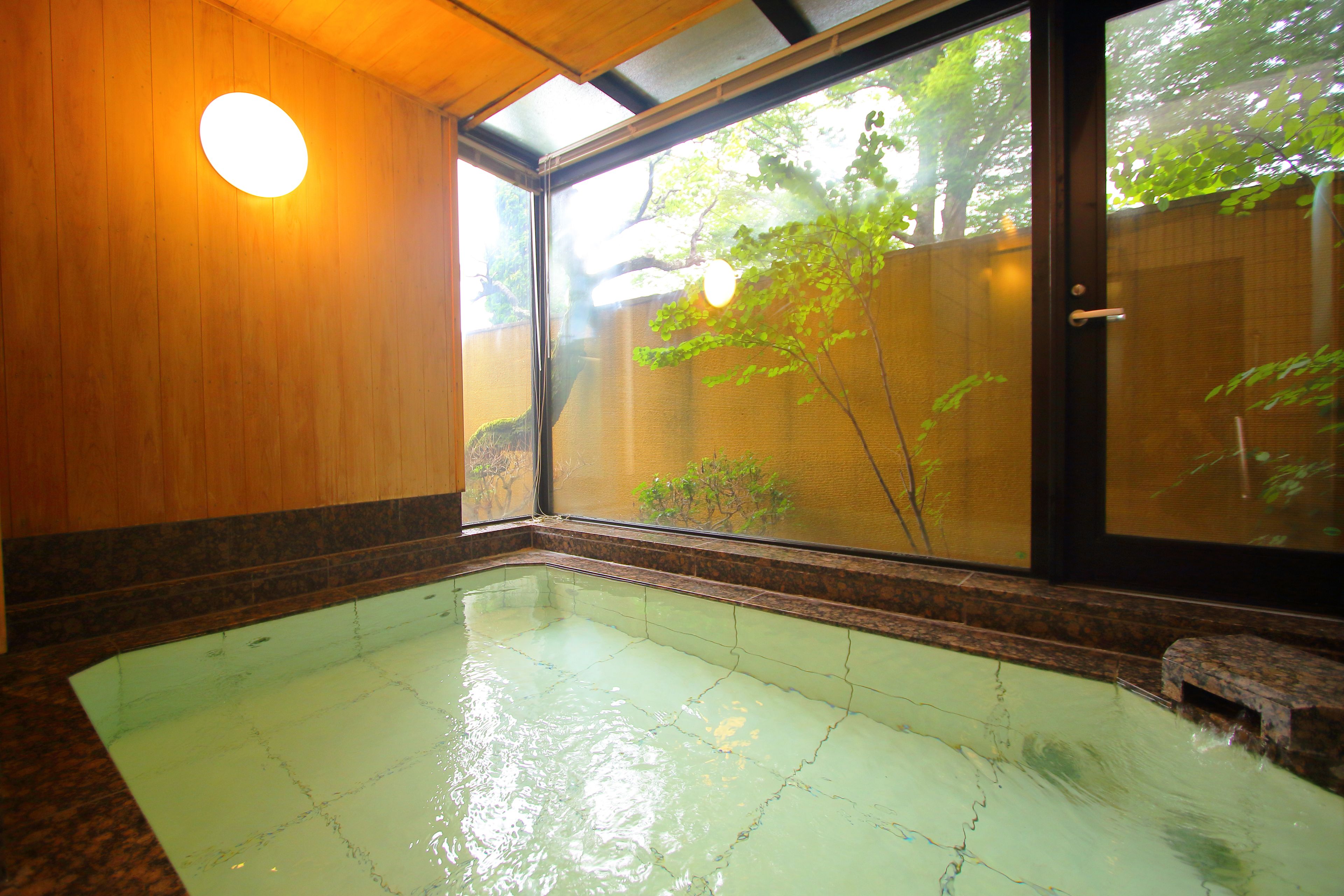 Un onsen japonés tradicional con interior de madera, un ventanal amplio y suelo de baldosas.