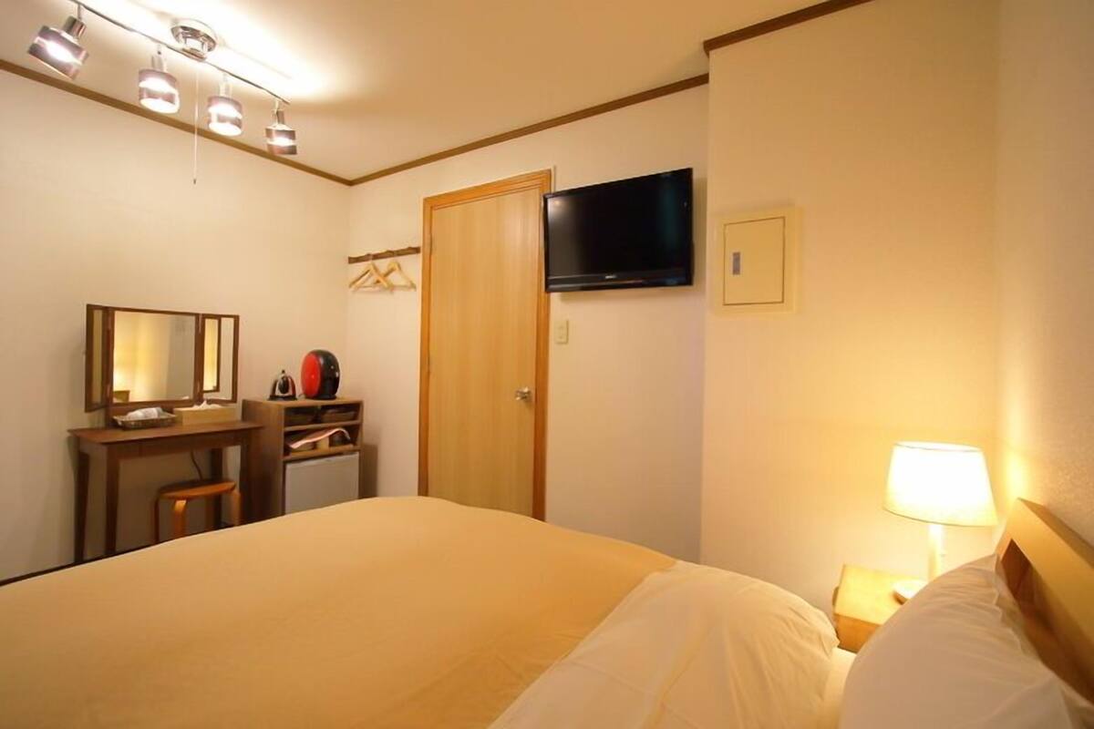 Hotellihuone, jossa on sänky, työpöytä tuolilla, televisio ja ovi.