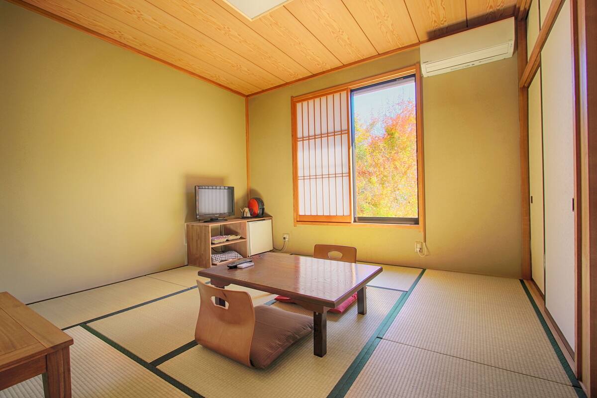 Perinteinen japanilainen huone, jossa on tatamimatto, matala pöytä ja televisio puukehikossa.