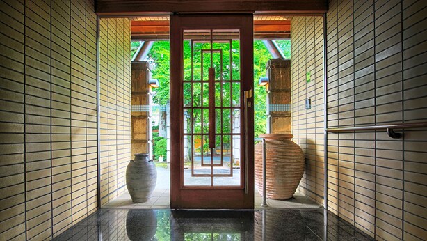 Un pasillo con paredes de azulejos, suelo pulido y una puerta de madera con celosía de metal.