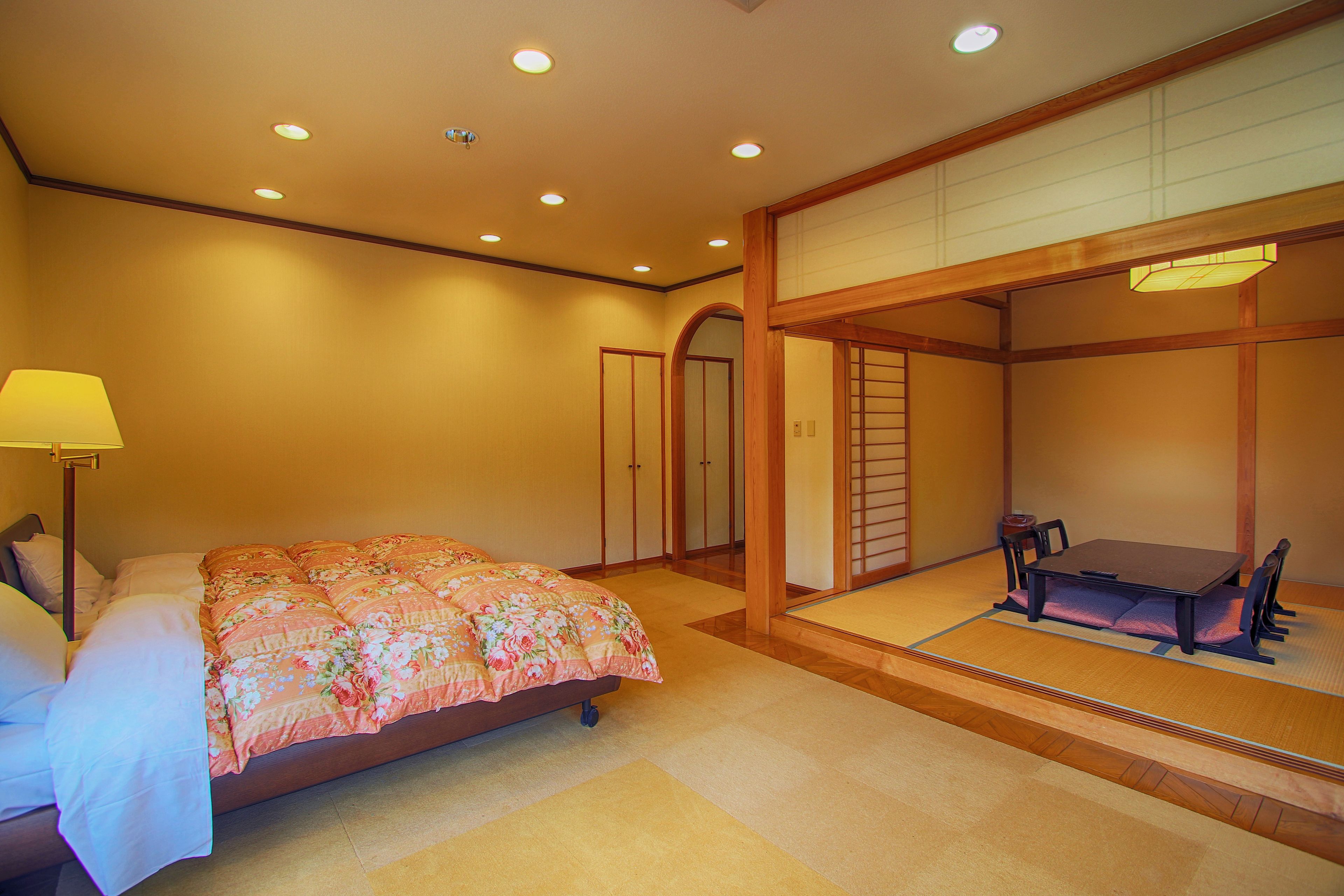 Un dormitorio de estilo japonés tradicional con cama, escritorio y un área de estar con esterillas de tatami.