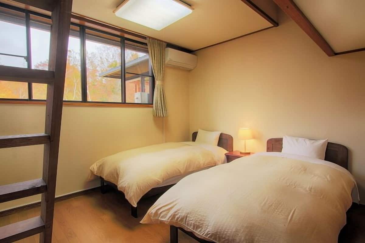 A bedroom with two beds, a wooden ladder, a window with curtains, and an air conditioning unit.
