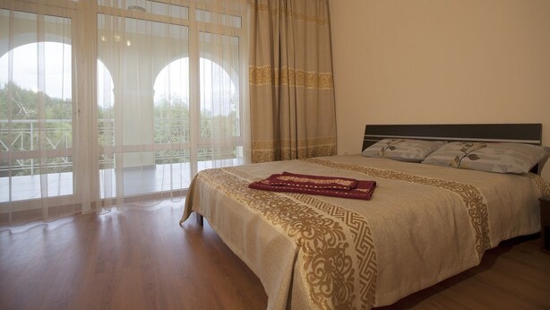 A bedroom with a large bed, a headboard, and a view through a window with curtains. - Hotel Aurora Plus (Bulan-Sogottu)