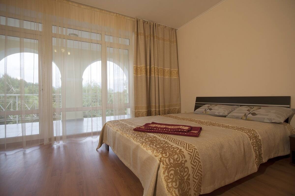 A bedroom with a large bed, a headboard, and a view through a window with curtains.