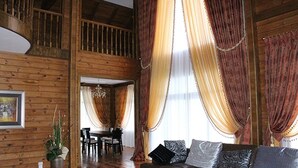 Amplia sala de estar con paredes de madera, un sofá con cojines estampados y un comedor con mesa y sillas.