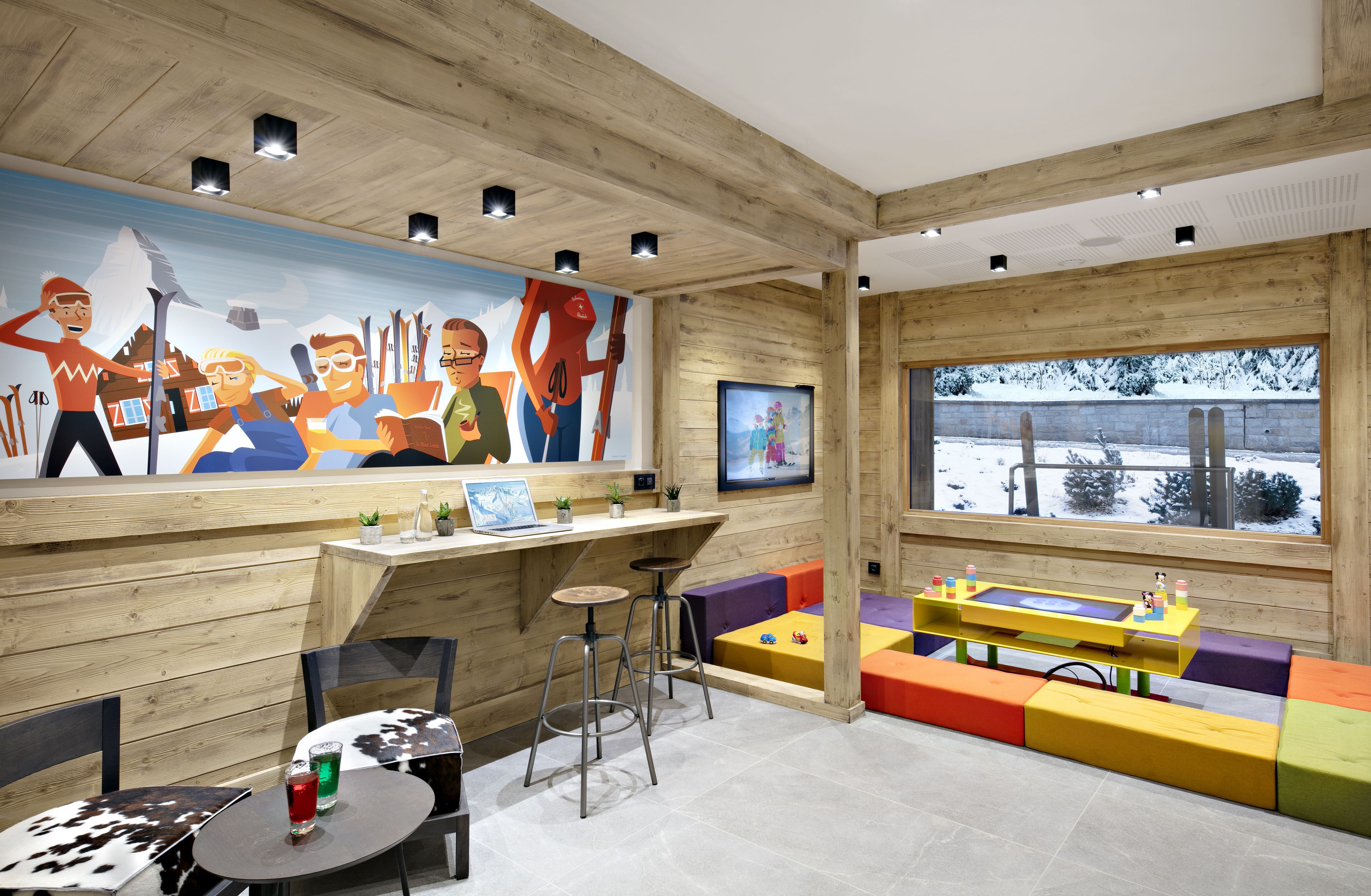 Un intérieur sur le thème du ski, avec des murs en bois, une fresque murale représentant des scènes de ski, un téléviseur et des sièges aux couleurs vives.