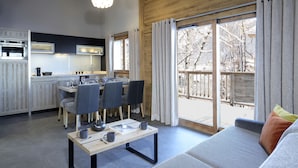 Una cocina moderna con electrodomésticos integrados, un comedor con mesa y sillas, y un amplio ventanal corredero que da a un espacio exterior.