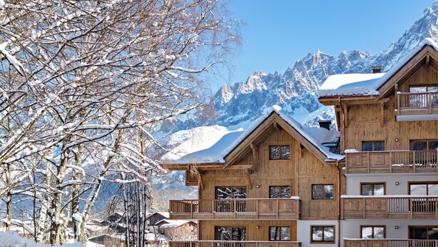 Una cabaña de madera con varios balcones, rodeada de árboles nevados y montañas.