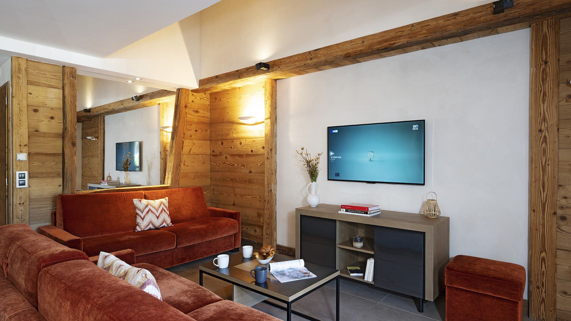 A modern living room with a red sofa, a coffee table, and a TV mounted on the wall.