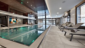 Una piscina interior moderna con sillones de descanso y vistas a la ciudad.
