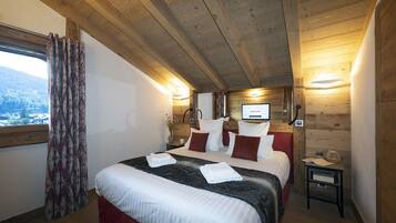A cozy bedroom with a wooden ceiling, a large bed with white and red bedding, a bedside table with a lamp, and a view of the outdoors through a window.