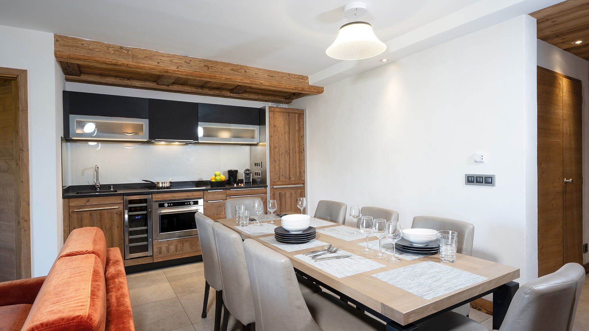 Une cuisine moderne avec des meubles en bois, un coin repas avec une table en bois dressée pour quatre personnes, et un coin salon confortable avec un canapé.