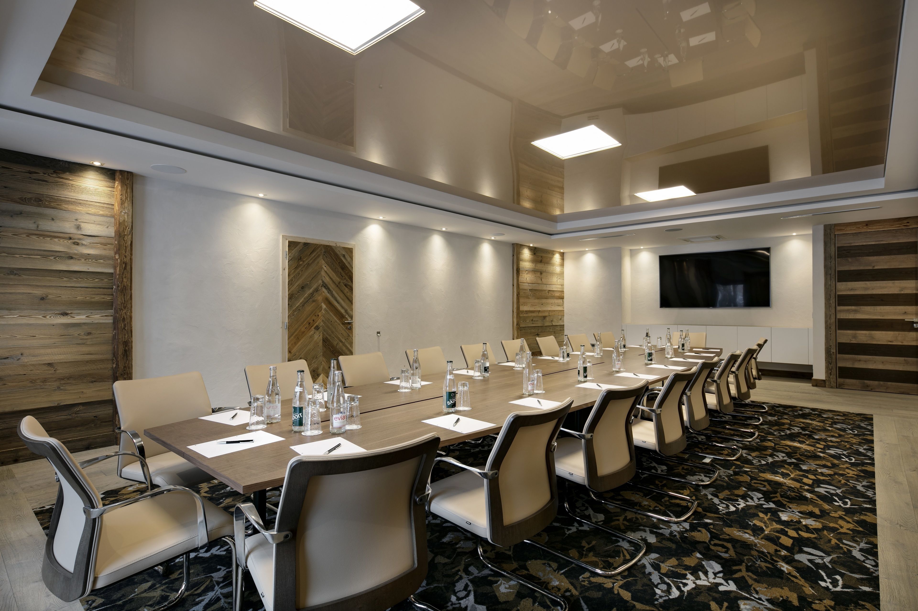 A conference room with a long table, chairs, water bottles, and a large screen.