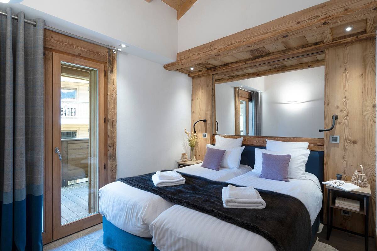 A bedroom with a large bed, wooden ceiling beams, a sliding glass door, and a nightstand with a lamp.