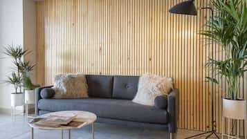A modern living room with a grey sofa, two fluffy cushions, a round coffee table, and a wooden slatted wall.