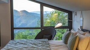 Un dormitorio con una ventana grande, una cama con ropa blanca, una silla y una lámpara de escritorio.