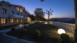 Un hotel con fachada de piedra, varias ventanas y un jardín bien iluminado con luces esféricas.