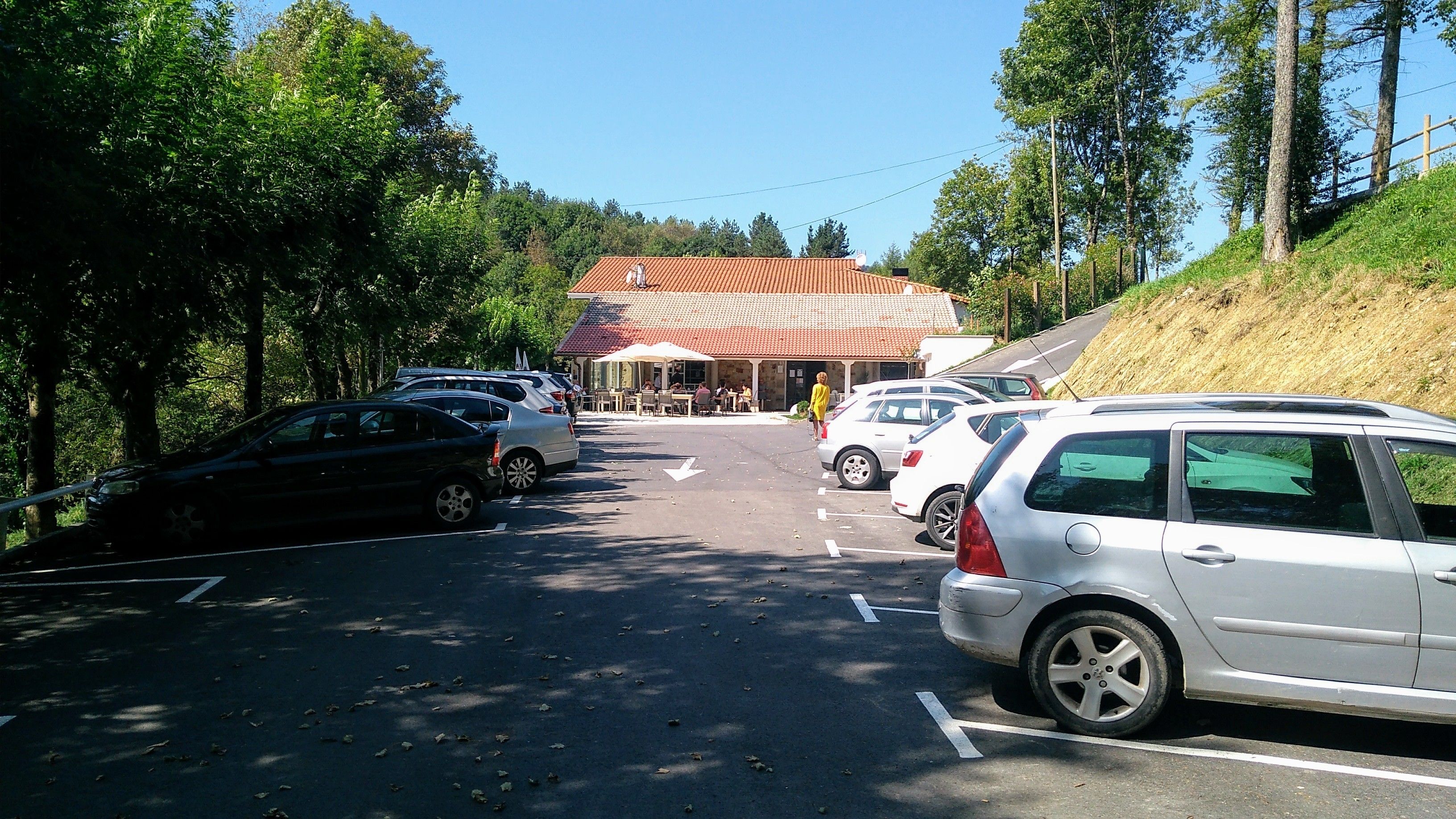 A parking lot with several cars, a building with a red roof, and trees in the background.
