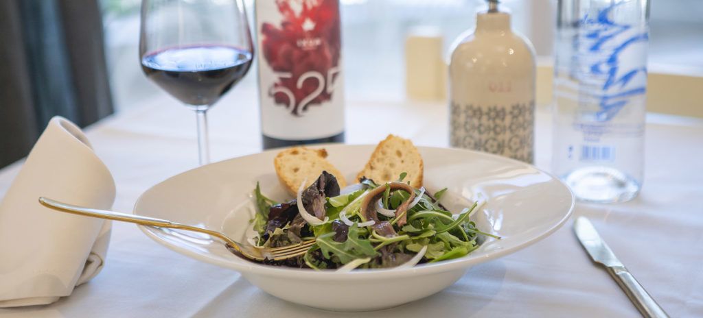 A dining table with a salad, bread, a wine glass, and a bottle of water.