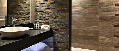 A bathroom with a stone wall, a large sink, and a mirror.