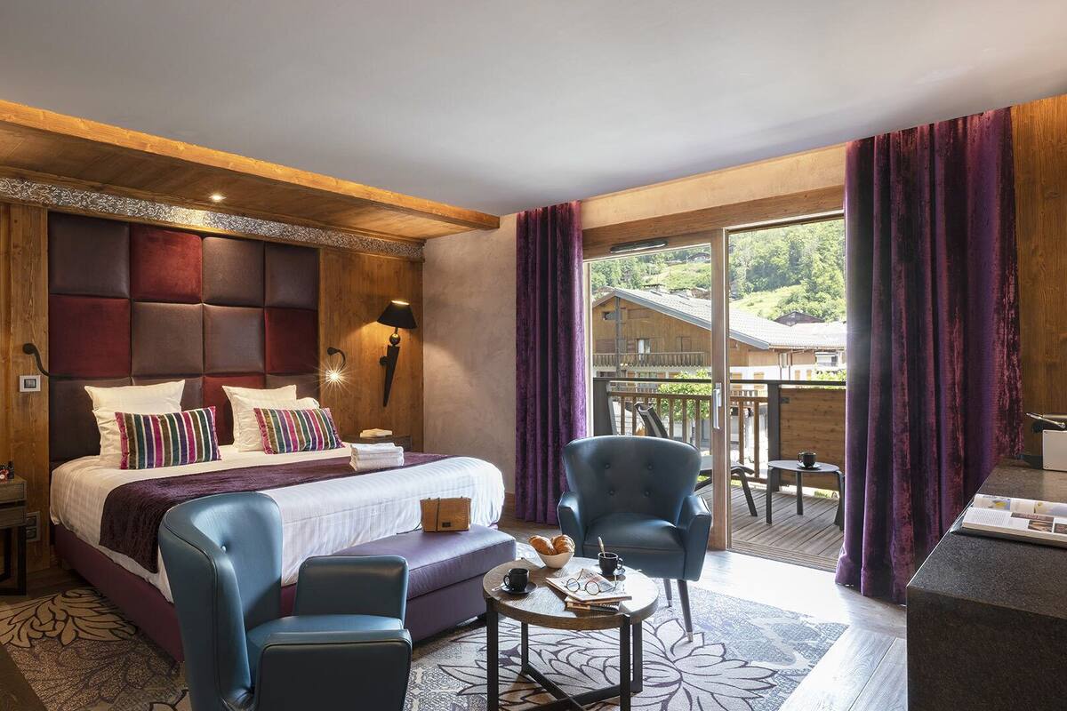 Habitación de hotel con una cama grande, dos sillones, una mesita y un balcón con vistas a los alrededores.