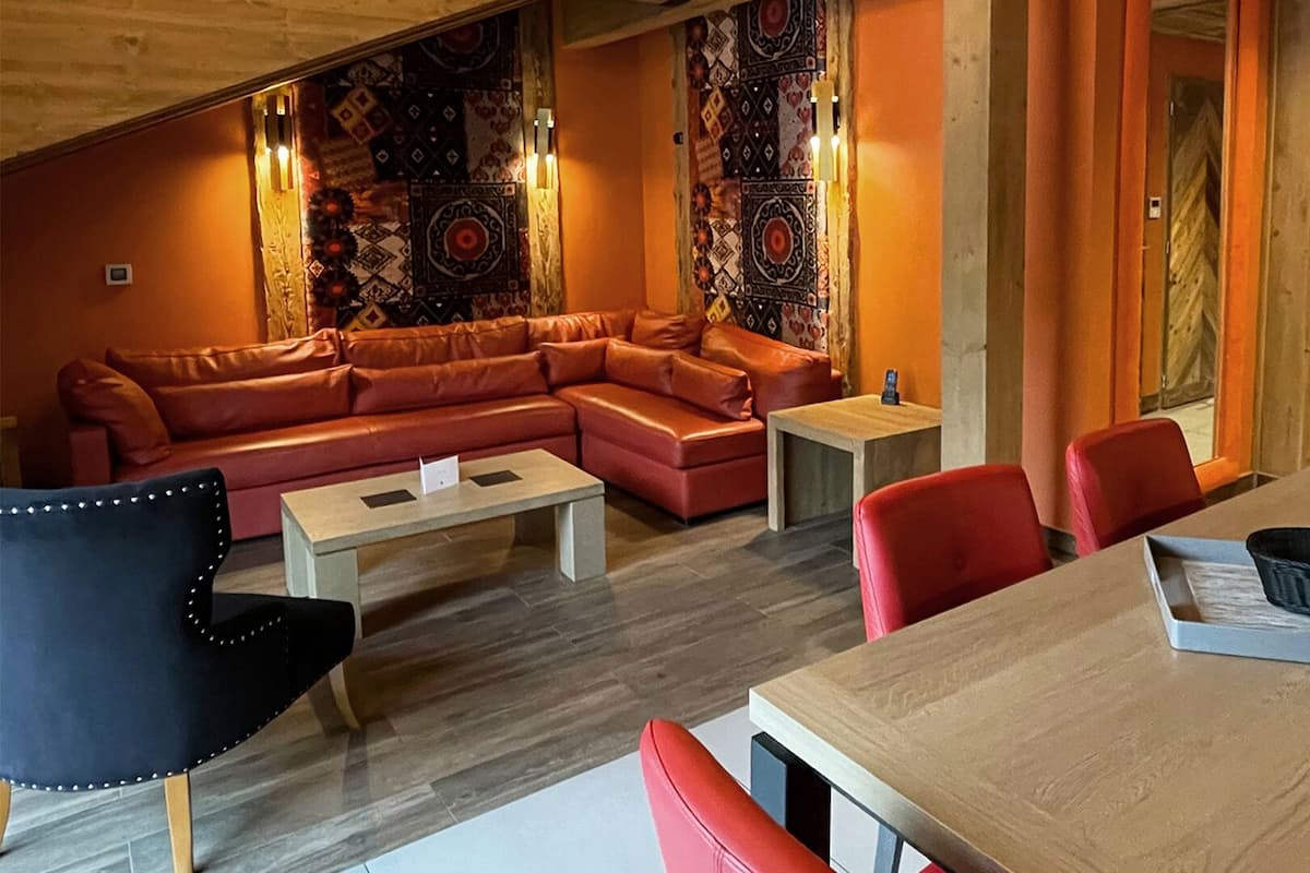 Amplia sala de estar con techo de madera, un sofá seccional grande, una mesa de comedor y sillas rojas.