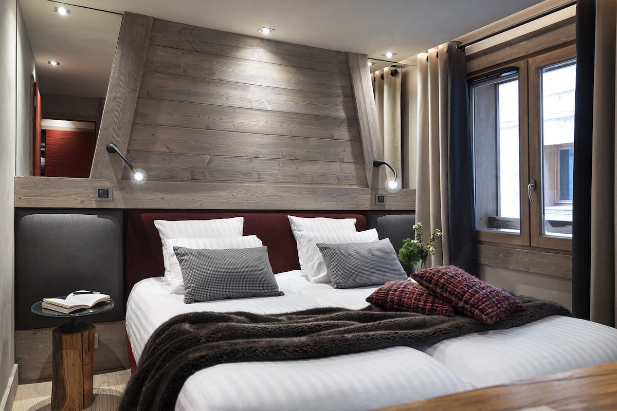 Un dormitorio con cama estilo altillo, una mesita de noche, una ventana con cortinas y vistas al exterior.