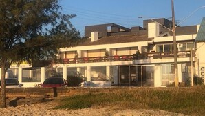 Un bâtiment à deux étages, doté d’un toit plat et de grandes fenêtres. On aperçoit un arbre au premier plan et une voiture garée devant.