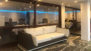 Un hall d’hôtel moderne avec un canapé blanc, de grandes fenêtres et un sol en marbre.