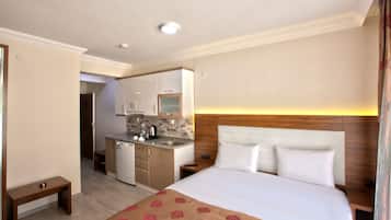 Una habitación de hotel con cama, mesitas de noche, un escritorio pequeño, kitchenette y baño.