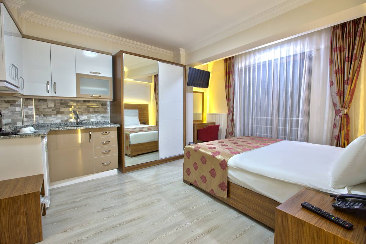 A hotel room with a bed, a bedside table with a remote control, a mirror, a TV, and a bathroom with a toilet and sink.