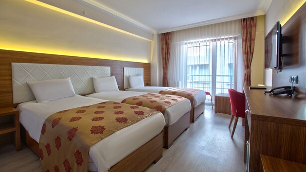 A hotel room with two beds, a desk with a chair, a TV, and a window with curtains. - Bolu Cadde Otel (Bolu)
